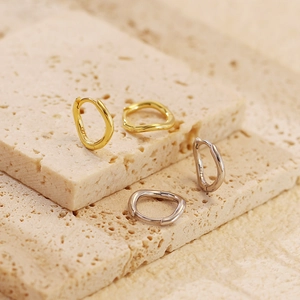 Macro view of gold and silver S925 irregular wavy hoop earrings on a stone base