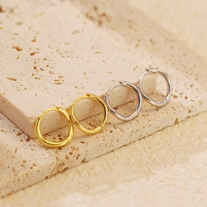 Close-up of wavy irregular silver and gold hoop earrings on a stone display surface