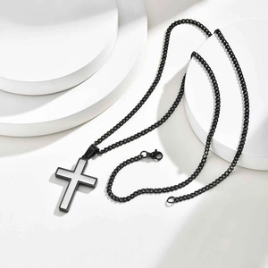 Minimalist black and silver stainless steel cross pendant necklace on a modern white stand