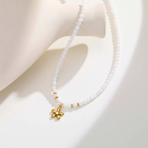 Détail d'un pendentif fleur dorée avec perles blanches sur un support minimaliste