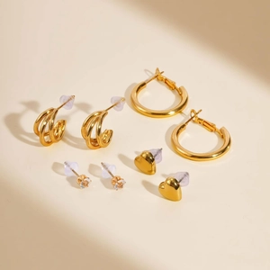 Detailansicht 4-teiliges vergoldetes Ohrring-Set mit Zirkon- und Herzsteckern auf Beige