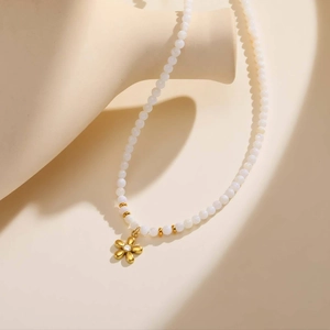 Détail de collier en perles blanches avec pendentif fleur dorée et zircon sur fond beige