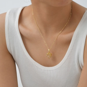 Detail shot of a rotating golden flower pendant with pink zircons on a delicate cross chain