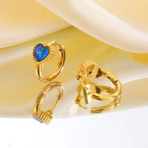 Detailweergave van gouden oorringen met blauwe hartvormige stenen op een zijden achtergrond
