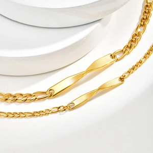 Detail of gold-plated Figaro chain bracelet with a twisted Möbius bar on white pedestal