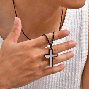 Detail of minimalist black and white cross pendant on a thin Cuban chain worn by model