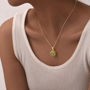 Detail of a rotating floral necklace with green zircons and gold-plated chain on a model
