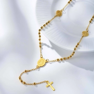 Dettaglio della collana a Y dorata con perline, medaglie religiose e ciondolo a croce classica