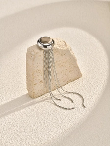 Close-up of a silver tassel ear cuff hanging on a textured stone display