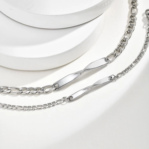 Detailed close-up of a silver Figaro chain bracelet with a twisted Mobius metal plate