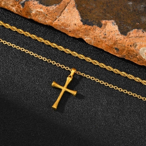 Vista de un colgante de cruz de acero inoxidable dorado con dos cadenas sobre una piedra