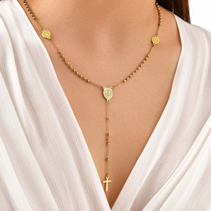 Dettaglio della collana a Y dorata con medaglie religiose e croce su un abito bianco