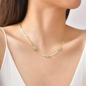 Dettaglio di una collana a catena serpente dorata con tre pietre turchesi ovali su modella