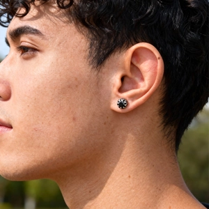 Gros plan d'un clou d'oreille rétro en acier titane avec motif soleil noir sur modèle