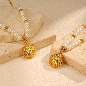 Detail of white pearls and gold beads necklace with sun and shell charms on stone