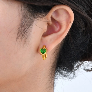 Detailopname van vergulde oorbel met hartvormige groene zirkoon gedragen door een model