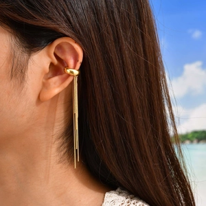Detailed close-up of a golden tassel ear cuff worn by a model on a beach backdrop
