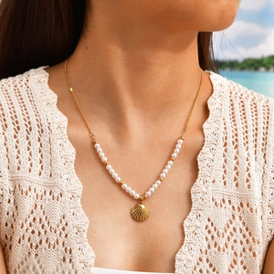 Golden pearl necklace with conch shell pendant worn by a model at the seaside beach