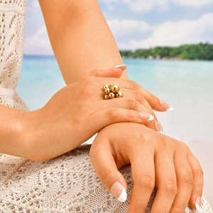 Golden stainless steel grape cluster bead ring worn by a model on a sunny beach background