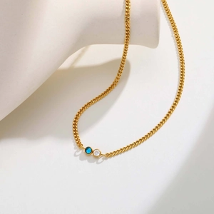Dettaglio di una collana a catena dorata sottile con pietre di zircone blu e bianche