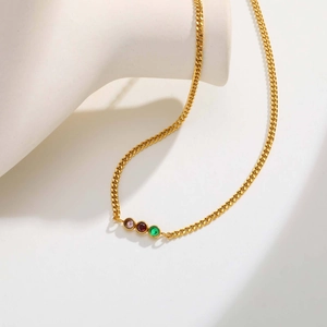 Dettaglio della collana a catena cubana dorata con tre zirconi colorati su un busto