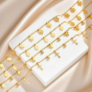 Detail von goldenen Edelstahlketten mit Schmetterling und Kreuz auf Seide
