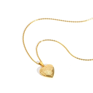 Close-up of golden heart locket necklace featuring detailed rose floral engraving pattern