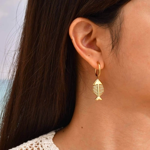 Golden stainless steel fishbone hoop earrings for women worn by model at the beach