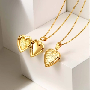 Detail of open and closed gold heart locket necklace with floral engraving on white display