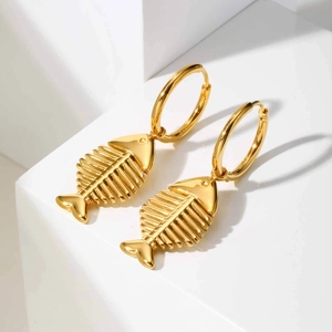 Golden fishbone hoop earrings made of polished stainless steel on white geometric blocks