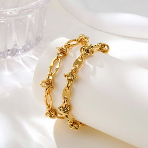 Vista dettagliata del bracciale dorato a maglie annodate su supporto bianco con ombre