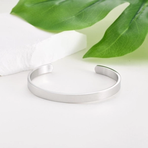 Minimalist silver stainless steel open C-shape cuff bracelet on a white stone background