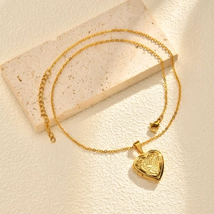 Detailed close-up of golden heart locket with rose engraving on a textured stone