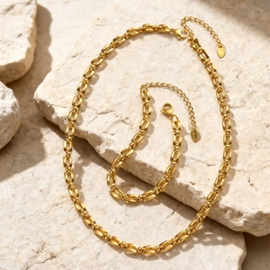 Elegante goudvergulde roestvrijstalen schakelketting en armband set op een natuursteen