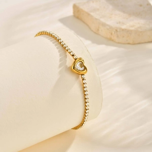 Dettaglio di un bracciale con ciondolo a cuore dorato e zirconi su un supporto cilindrico