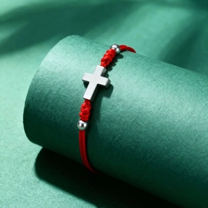 Macro detail of red woven rope bracelet with metallic cross charm and silver beads