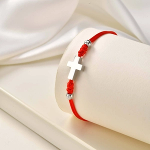 Macro shot of red braided rope bracelet with polished steel cross on a white display