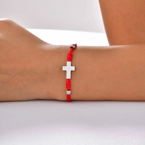 Detail of red woven polyester cord bracelet with silver cross pendant on wrist