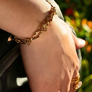 Elegante bracciale dorato con nodi e maglie ovali indossato da una modella al sole