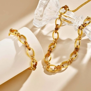 Dettaglio di collana e bracciale dorati con maglie in resina marrone su base bianca