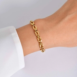 Detailopname van een gouden roestvrijstalen geometrische schakelarmband om de pols