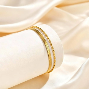 Detail of layered gold snake chain and beaded bracelet on elegant champagne satin