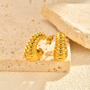 Macro detail of golden twisted hoop earrings with polished metallic luster on stone