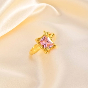 Macro view of rectangular pink zircon ring with gold star accents on silk fabric