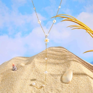 Detail of gold Y-shaped necklace with white pearls and flower charm on sandy beach