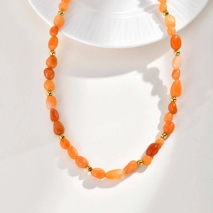 Close-up of handmade necklace with orange natural stones and gold beads on white plate