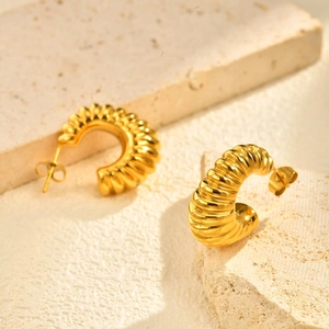 Macro detail of golden ribbed croissant earrings on a natural stone display stand