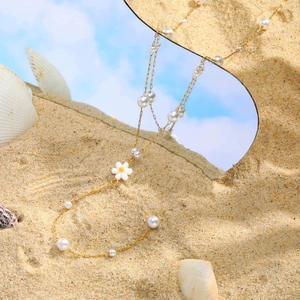 Golden Y-shaped pearl necklace with white daisy pendant on a sandy beach setting