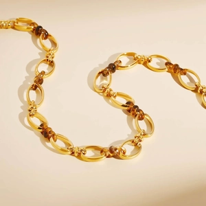 Dettaglio catena dorata in acciaio inossidabile con maglie in resina ambra su sfondo beige