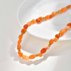 Detailed shot of orange agate beads and golden metal spheres on a white ceramic plate